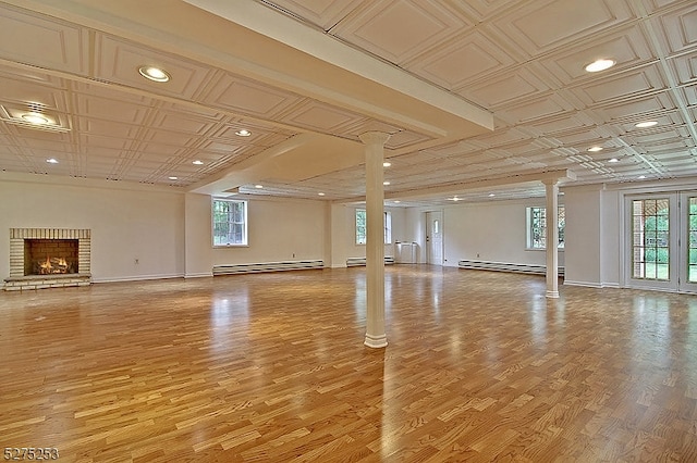 workout room with light wood-type flooring, a baseboard heating unit, a fireplace, and ornate columns