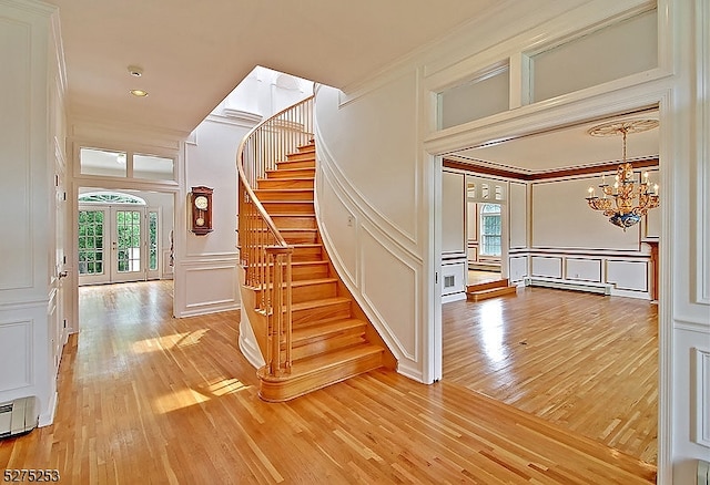 staircase with a chandelier, a baseboard heating unit, french doors, light hardwood / wood-style flooring, and crown molding