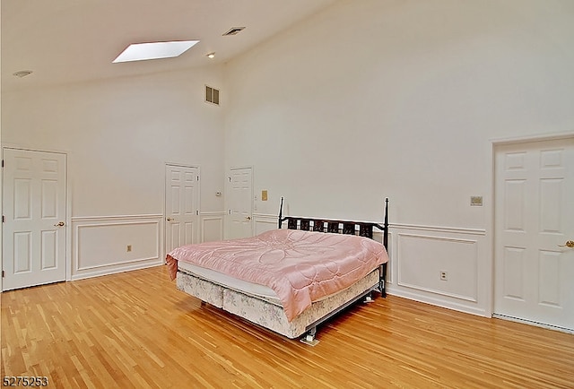 bedroom with high vaulted ceiling, light hardwood / wood-style floors, and a skylight