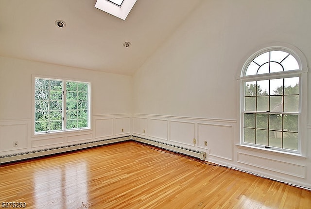 spare room featuring a skylight, high vaulted ceiling, a baseboard heating unit, and light hardwood / wood-style flooring