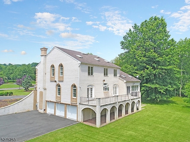 rear view of property with a balcony, a garage, and a yard