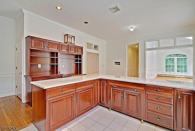 kitchen with ornamental molding, kitchen peninsula, light stone counters, and light hardwood / wood-style flooring