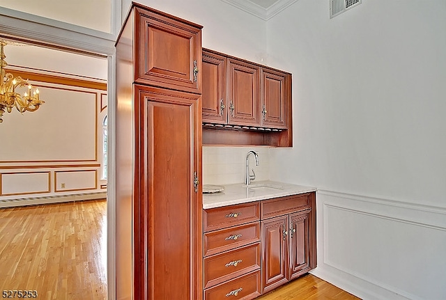 kitchen with light wood-type flooring, paneled built in fridge, a notable chandelier, sink, and crown molding