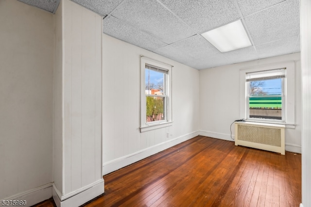 unfurnished room with a paneled ceiling, dark wood-type flooring, and radiator heating unit