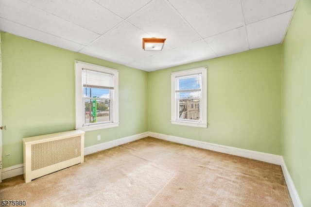 unfurnished room featuring light carpet, a drop ceiling, and radiator heating unit