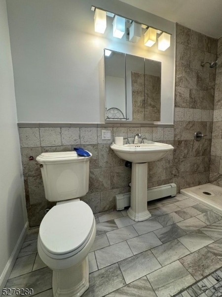 bathroom with a tile shower, tile walls, and toilet