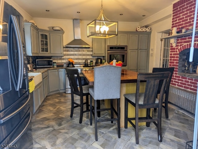 kitchen featuring appliances with stainless steel finishes, wall chimney exhaust hood, backsplash, crown molding, and pendant lighting