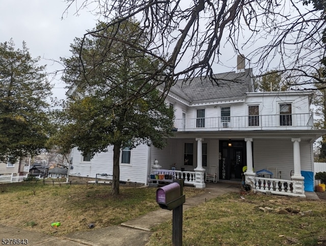 view of front facade with covered porch, a balcony, and a front lawn