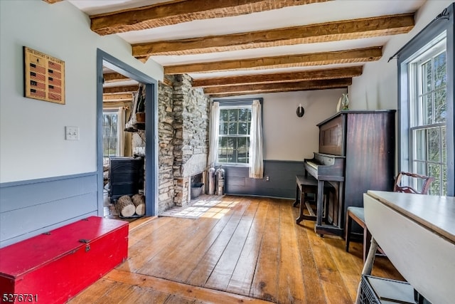 misc room with light wood-type flooring, a fireplace, and beamed ceiling