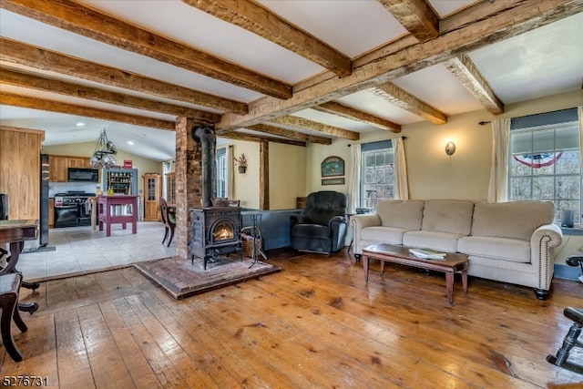 living room with a healthy amount of sunlight, a wood stove, wood-type flooring, and lofted ceiling with beams