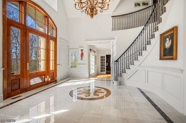 tiled foyer entrance with a high ceiling, french doors, and a notable chandelier