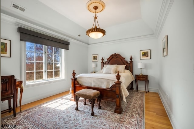 bedroom with ornamental molding, wood-type flooring, and a raised ceiling