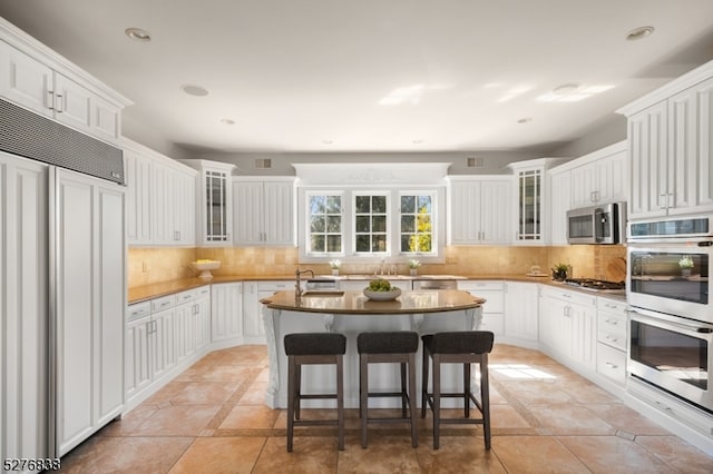 kitchen featuring white cabinets, appliances with stainless steel finishes, tasteful backsplash, and light tile floors