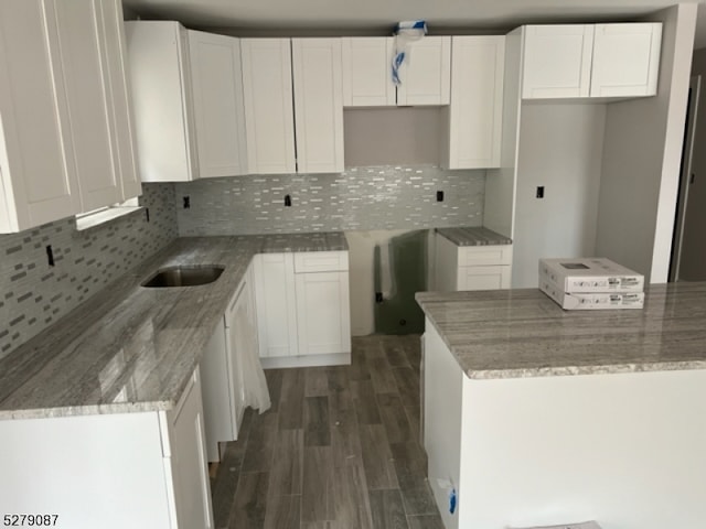 kitchen with dark wood-type flooring, white cabinetry, light stone counters, and decorative backsplash