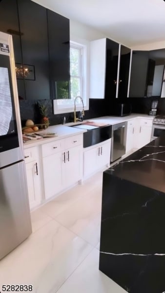 kitchen with white stove, stainless steel fridge, light tile floors, and white cabinetry