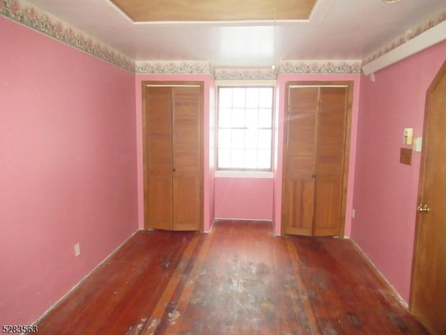 unfurnished bedroom featuring a tray ceiling, hardwood / wood-style floors, and two closets