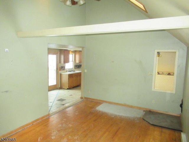 interior space featuring baseboards, high vaulted ceiling, a sink, and light wood-style floors