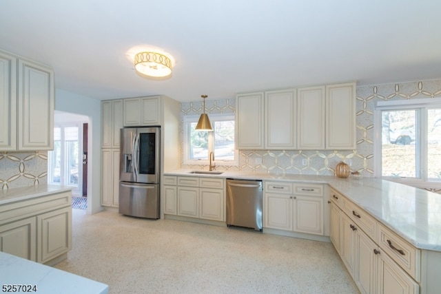 kitchen featuring sink, hanging light fixtures, stainless steel appliances, backsplash, and cream cabinetry