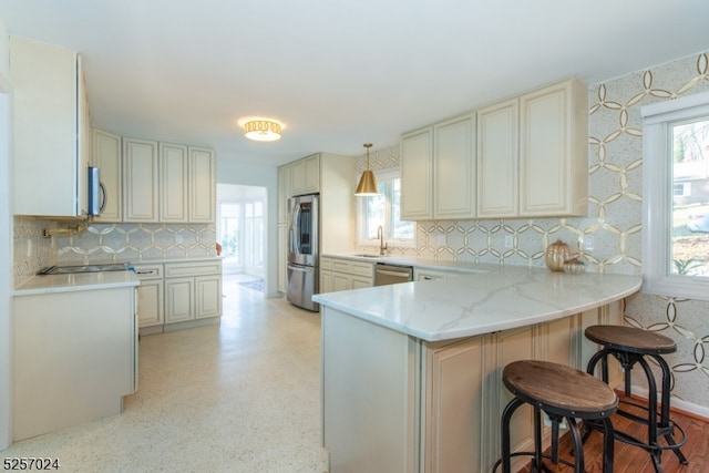 kitchen with kitchen peninsula, appliances with stainless steel finishes, a kitchen breakfast bar, a healthy amount of sunlight, and pendant lighting