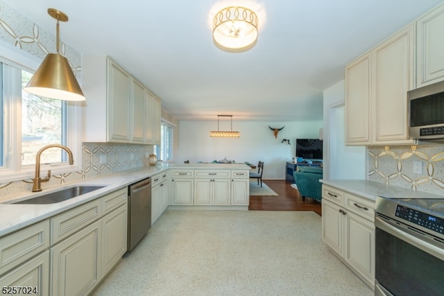 kitchen featuring sink, stainless steel appliances, hanging light fixtures, cream cabinetry, and decorative backsplash