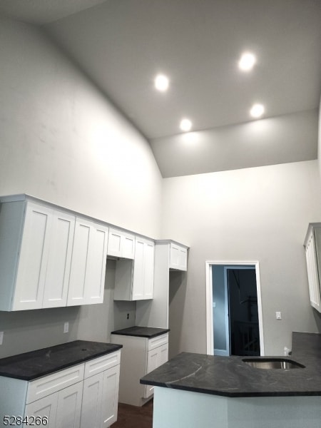 kitchen with kitchen peninsula, vaulted ceiling, sink, and white cabinetry