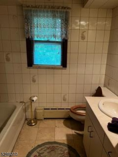 bathroom featuring a baseboard heating unit, tile floors, tile walls, vanity, and toilet