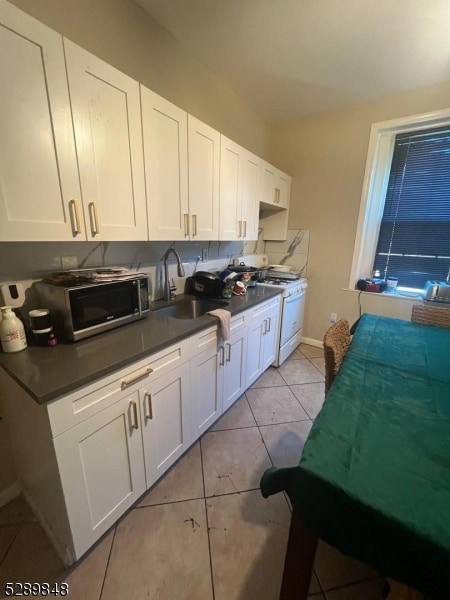 kitchen featuring sink, white gas range oven, light tile flooring, and white cabinetry