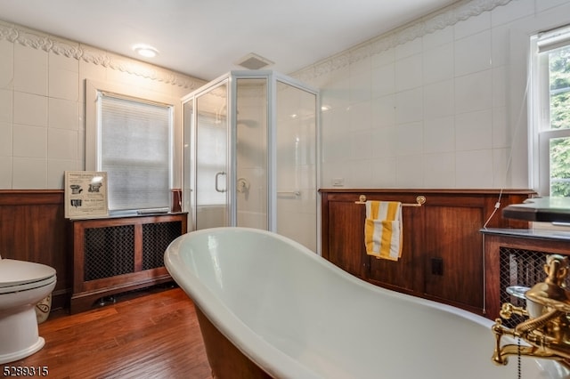 bathroom featuring hardwood / wood-style floors, tile walls, independent shower and bath, radiator heating unit, and toilet