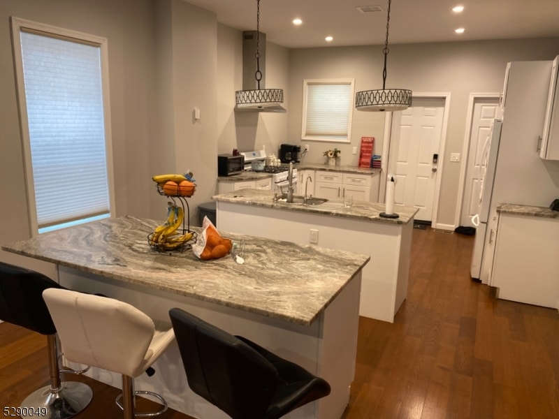 kitchen with wall chimney range hood, dark hardwood / wood-style flooring, a kitchen island, white cabinets, and pendant lighting