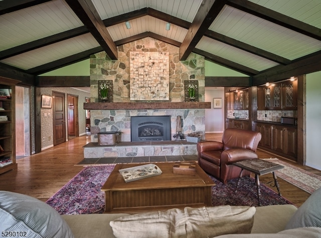 living room featuring high vaulted ceiling, beamed ceiling, hardwood / wood-style floors, and a stone fireplace