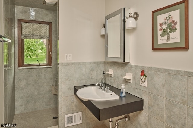 bathroom featuring tiled shower, sink, tasteful backsplash, and tile walls