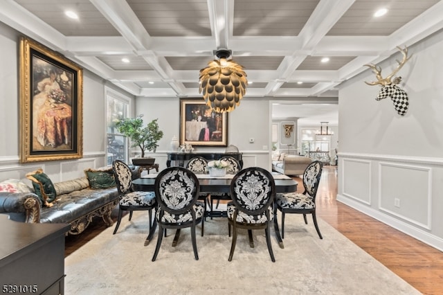 dining space with beam ceiling, coffered ceiling, light hardwood / wood-style flooring, and a chandelier