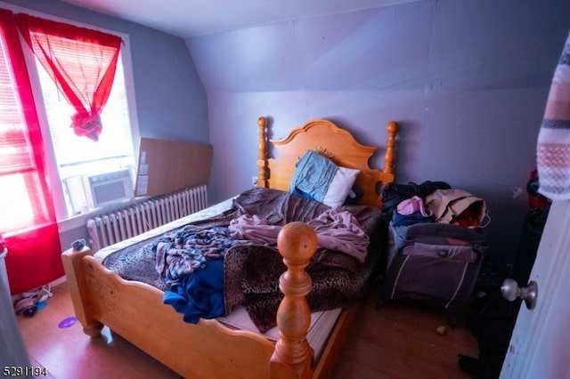 bedroom featuring vaulted ceiling, wood-type flooring, radiator, and multiple windows