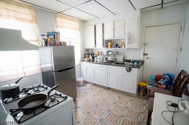 kitchen with tasteful backsplash, white gas range, sink, white cabinets, and stainless steel refrigerator