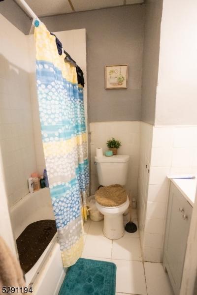 bathroom featuring tile patterned floors, a shower with curtain, toilet, and tile walls