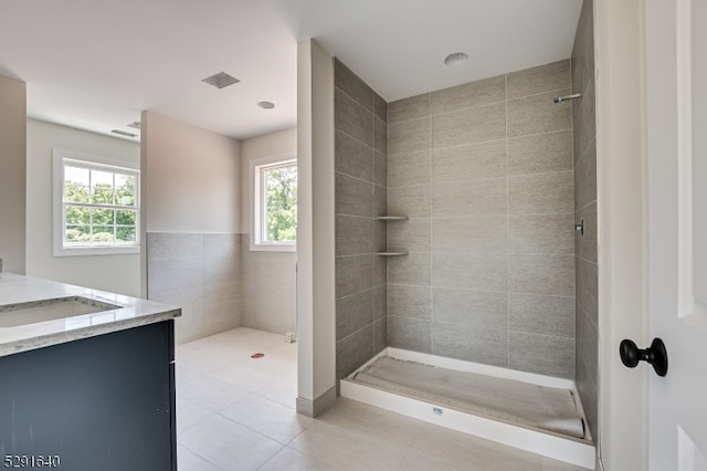 bathroom featuring a tile shower, vanity, tile walls, and a healthy amount of sunlight