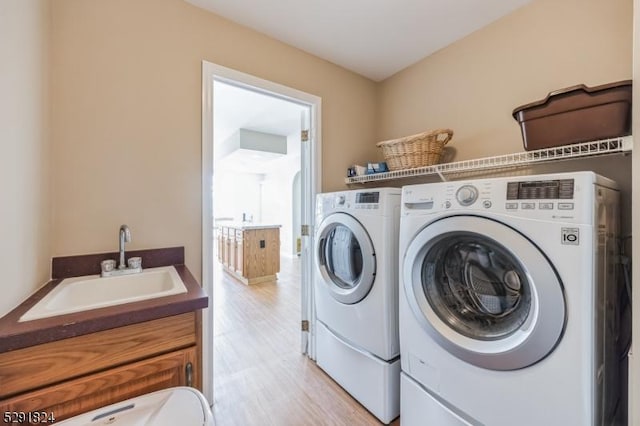 clothes washing area featuring separate washer and dryer, sink, and light wood-type flooring