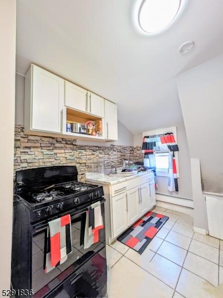 kitchen with black range with gas stovetop, light tile patterned floors, a baseboard radiator, white cabinets, and lofted ceiling