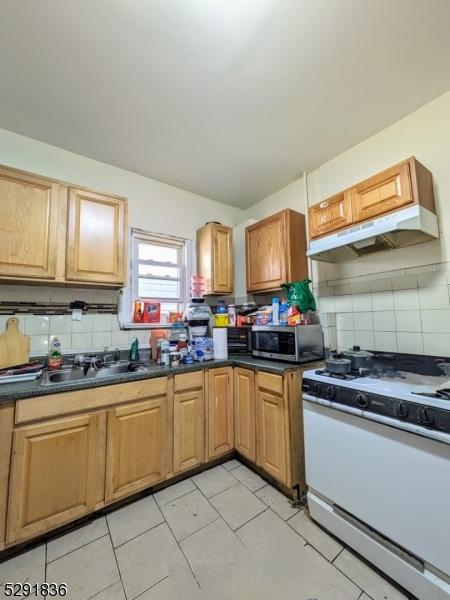 kitchen with white gas range, sink, tasteful backsplash, light tile patterned floors, and exhaust hood