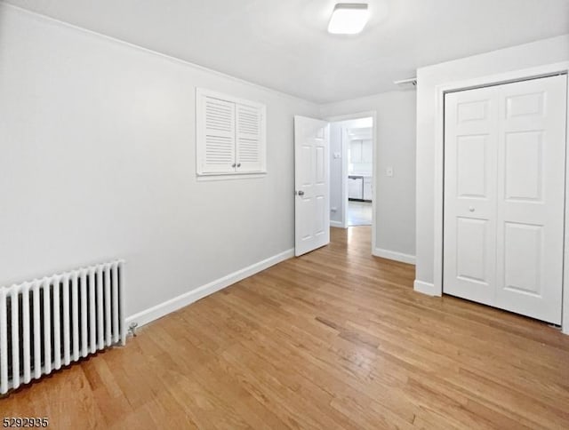 unfurnished bedroom featuring light wood-type flooring, radiator, and a closet