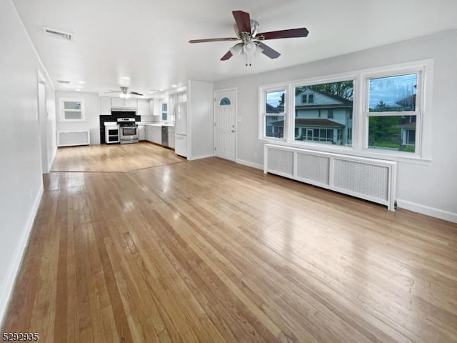 unfurnished living room featuring ceiling fan, radiator heating unit, and light hardwood / wood-style flooring