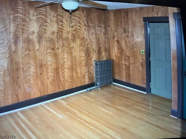 empty room with hardwood / wood-style flooring, ceiling fan, and wood walls