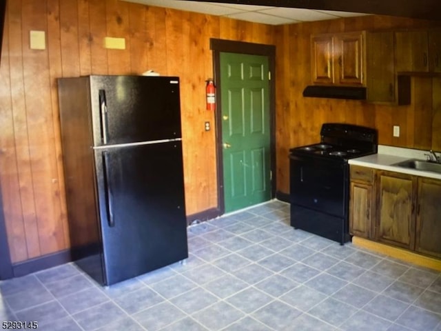 kitchen with sink, light tile patterned floors, wooden walls, and black appliances