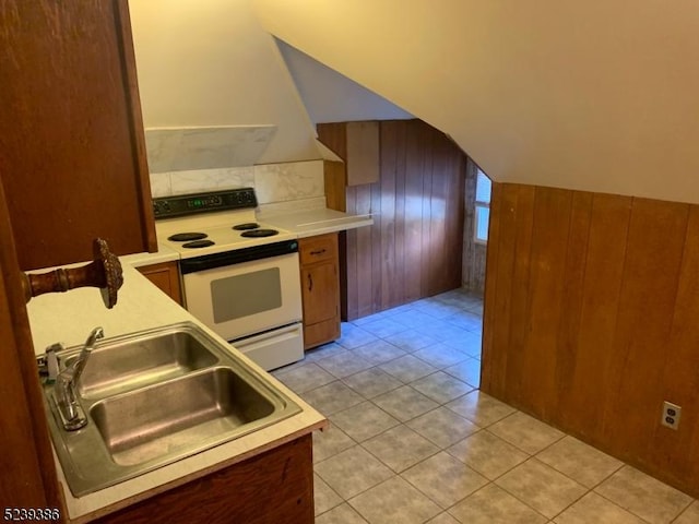 kitchen featuring vaulted ceiling, wooden walls, sink, light tile patterned floors, and electric range