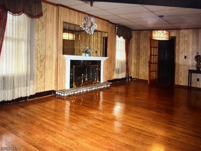 unfurnished living room featuring hardwood / wood-style flooring, a high end fireplace, a drop ceiling, and wood walls