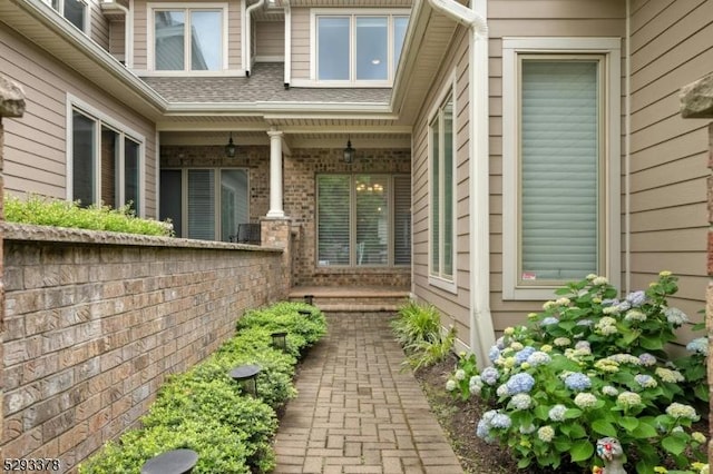 doorway to property with roof with shingles and brick siding