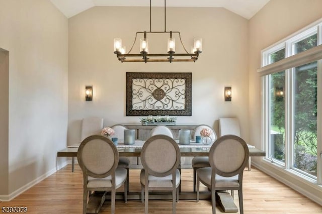 dining space with lofted ceiling, light wood-style floors, a healthy amount of sunlight, and a notable chandelier