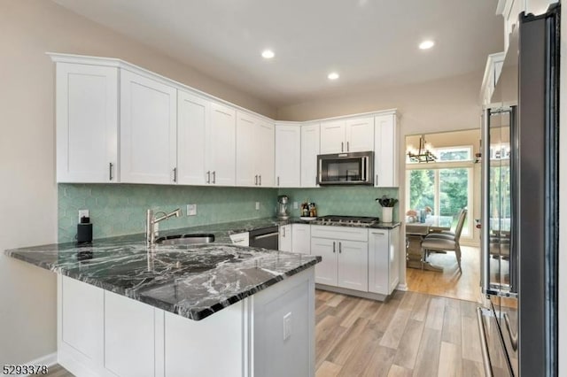 kitchen featuring light wood finished floors, appliances with stainless steel finishes, white cabinets, dark stone countertops, and a peninsula