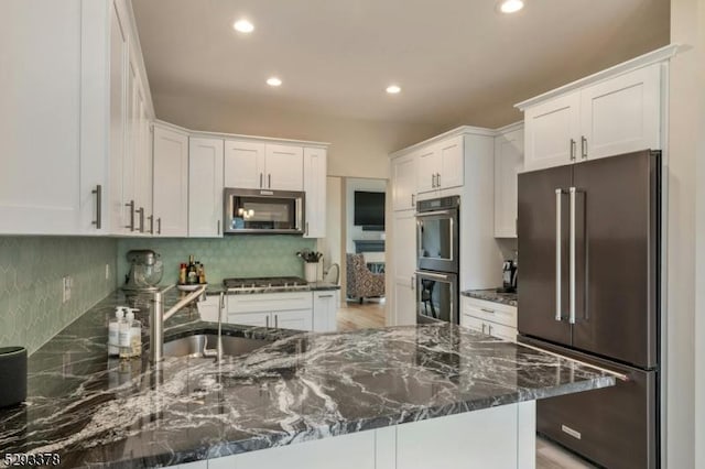 kitchen with appliances with stainless steel finishes, dark stone countertops, a peninsula, white cabinetry, and backsplash