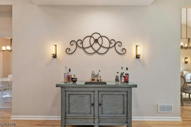 bar with a chandelier, a dry bar, light wood-style flooring, and visible vents